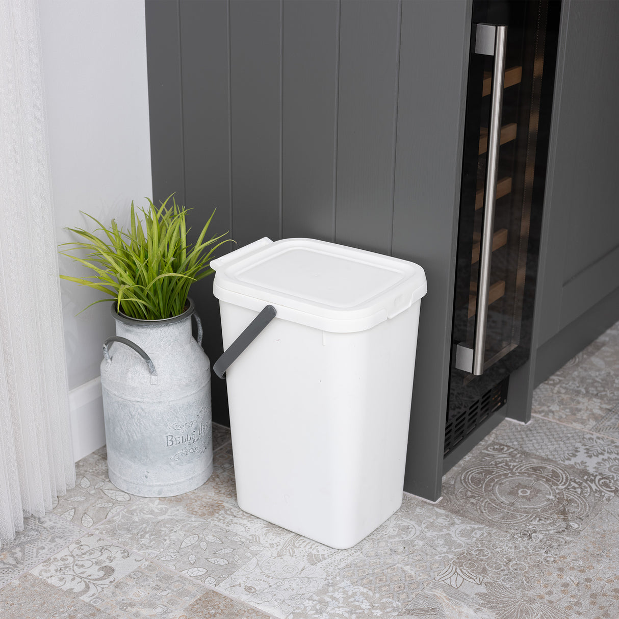 Small white utility caddy next to a grey cupboard with a plant in a metal pot.