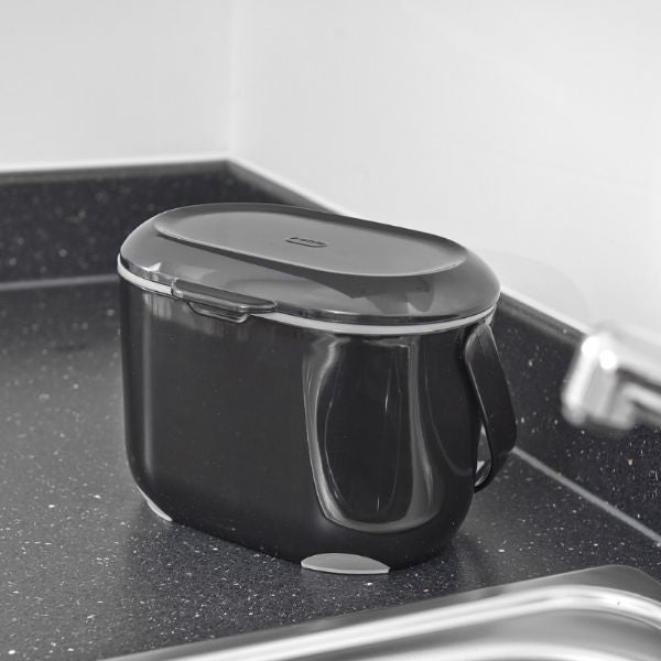 Black plastic compost caddy sitting on a black worktop in a kitchen by a sink