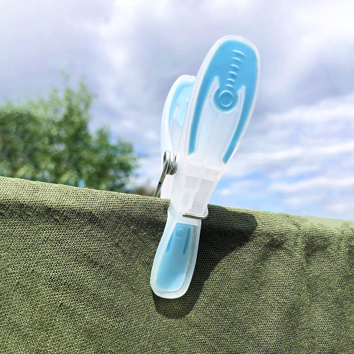 Blue and clear clothes peg holding a green clothing item on the clothes line, with cloudy sky background