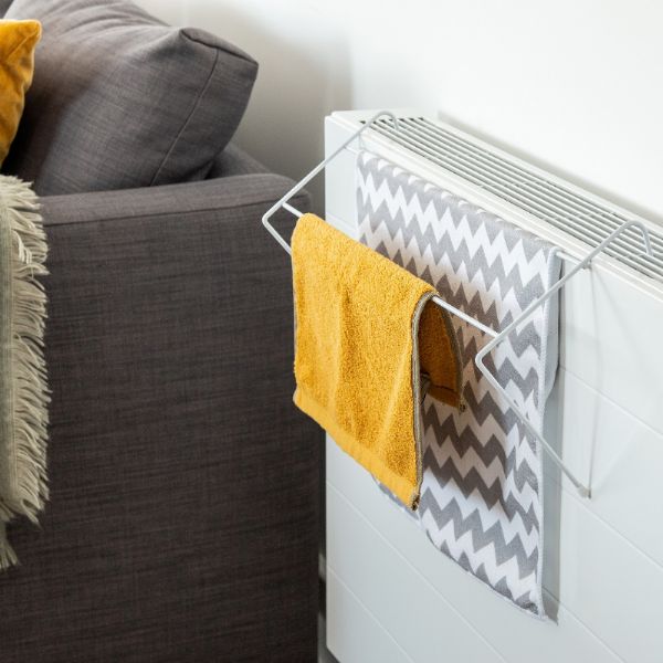 Radiator with towel rack holding yellow and patterned towels next to a sofa.