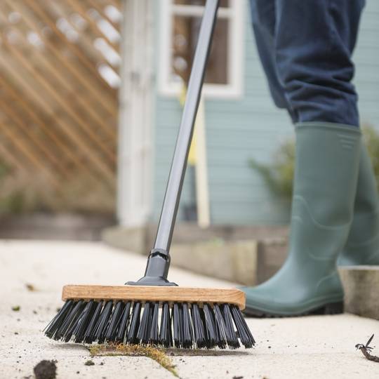 Person cleaning with a stiff bristled broom in outdoor setting
