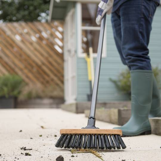 Person cleaning pathway with a stiff bristled broom in a garden setting