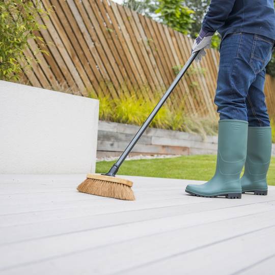 Person cleaning a patio with a broom in a garden setting with green wellington boots on.