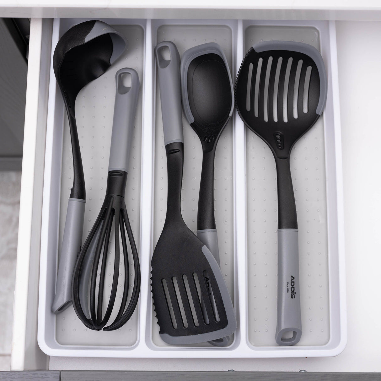 Set of black kitchen utensils in a white drawer organiser.