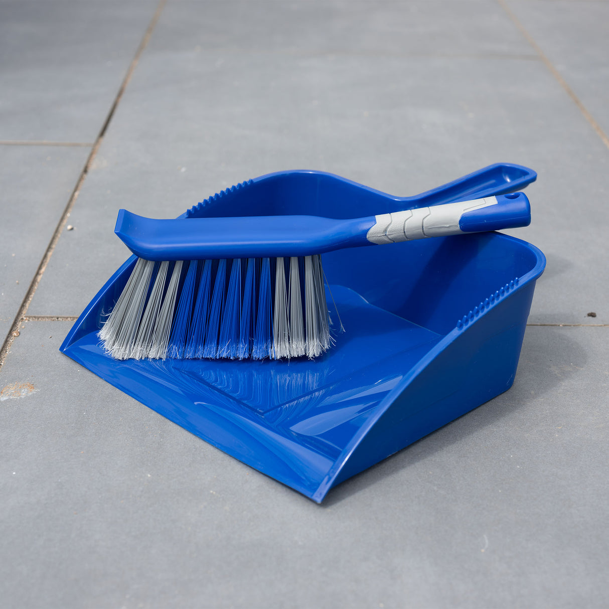 Blue dustpan and brush set on a gray tiled patio floor