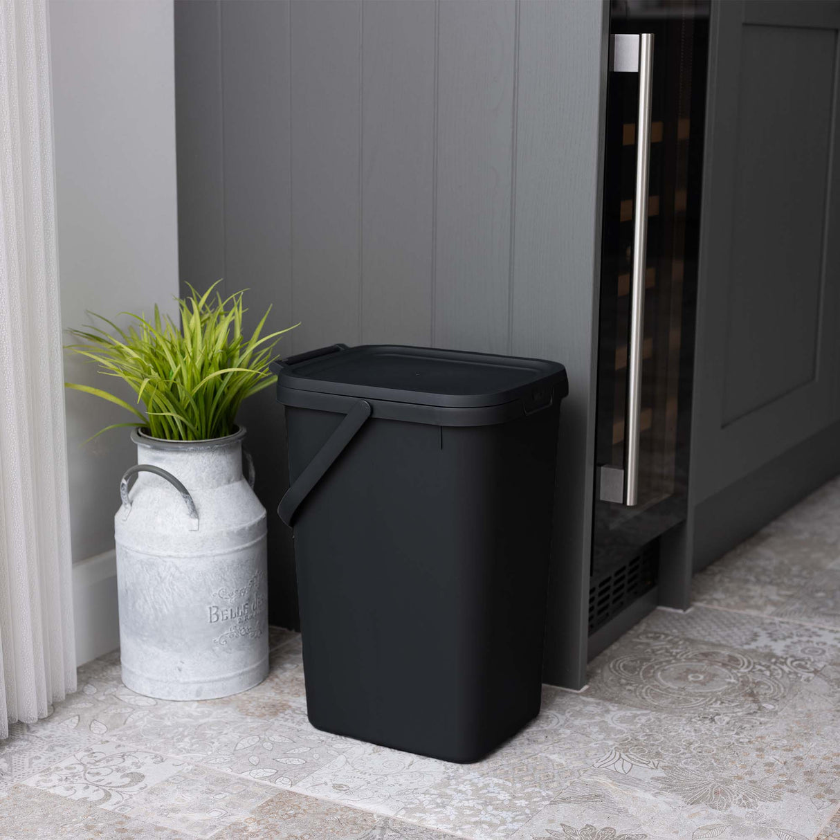 Small black utility caddy next to a grey cupboard with a plant in a metal pot.