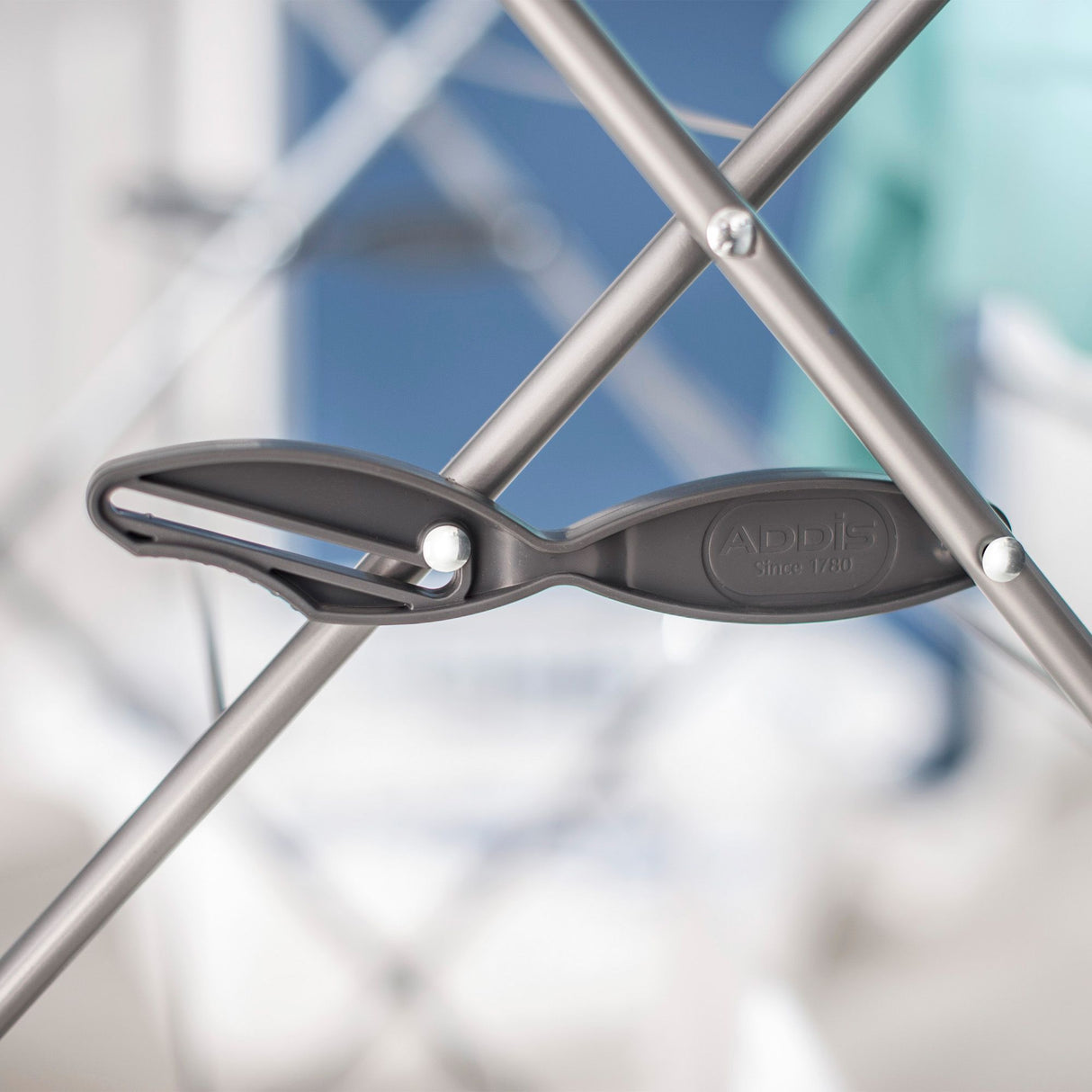 Close-up of a metal and plastic hinge on a clothes drying rack with a blurred background.