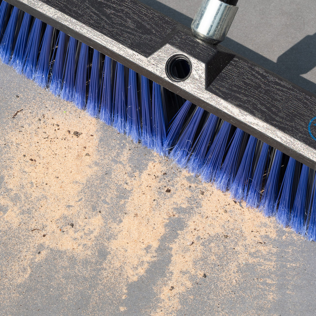 Cleaning brush with blue bristles sweeping grit and dirt from a patio