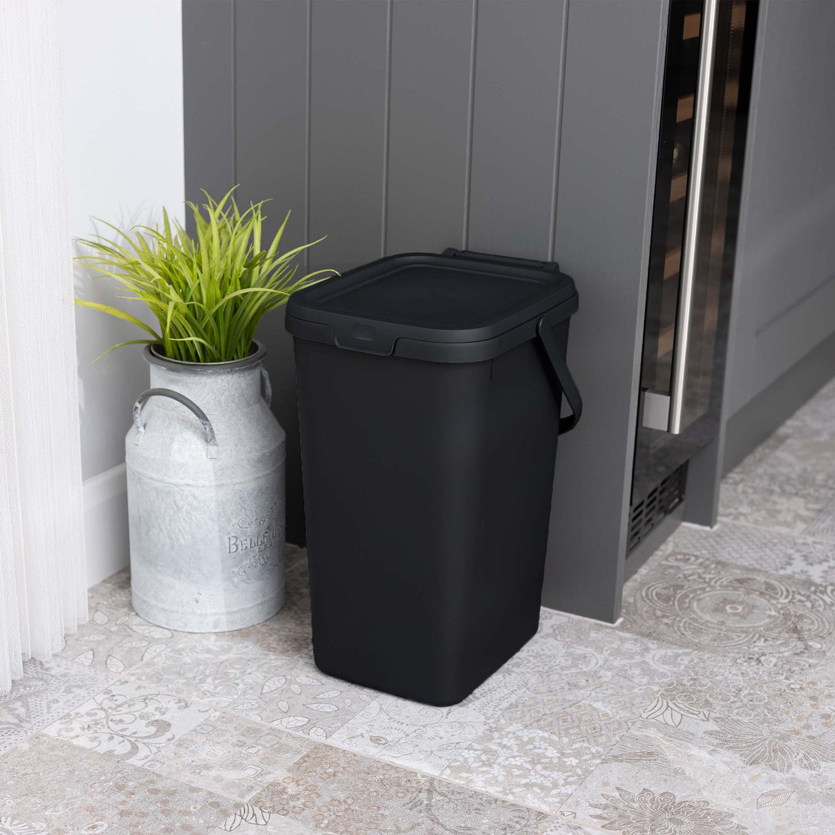 Small black utility caddy next to a grey cupboard with a plant in a metal pot.