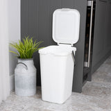 White utility caddy with lid open waiting to be used for recycling, next to a grey cupboard and plant in metal pot.