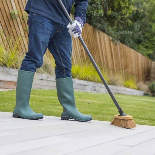 Person in green rubber boots using a broom on a patio.