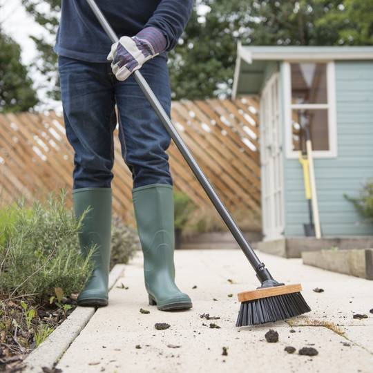 Person in green wellington boots using a broom to clean a path outdoors.