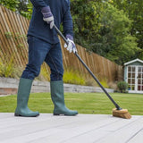 Person in green wellington boots cleaning a deck with a broom.