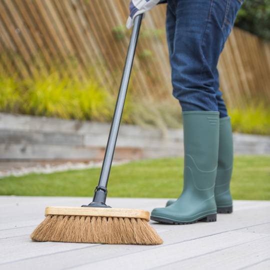 Person cleaning with a broom in garden setting wearing green wellington boots.