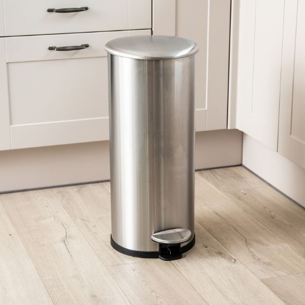 Stainless steel pedal bin on a wooden floor in a kitchen.
