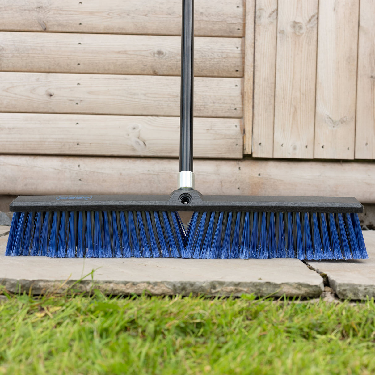 Garden broom with blue bristles leaning against a wooden fence.
