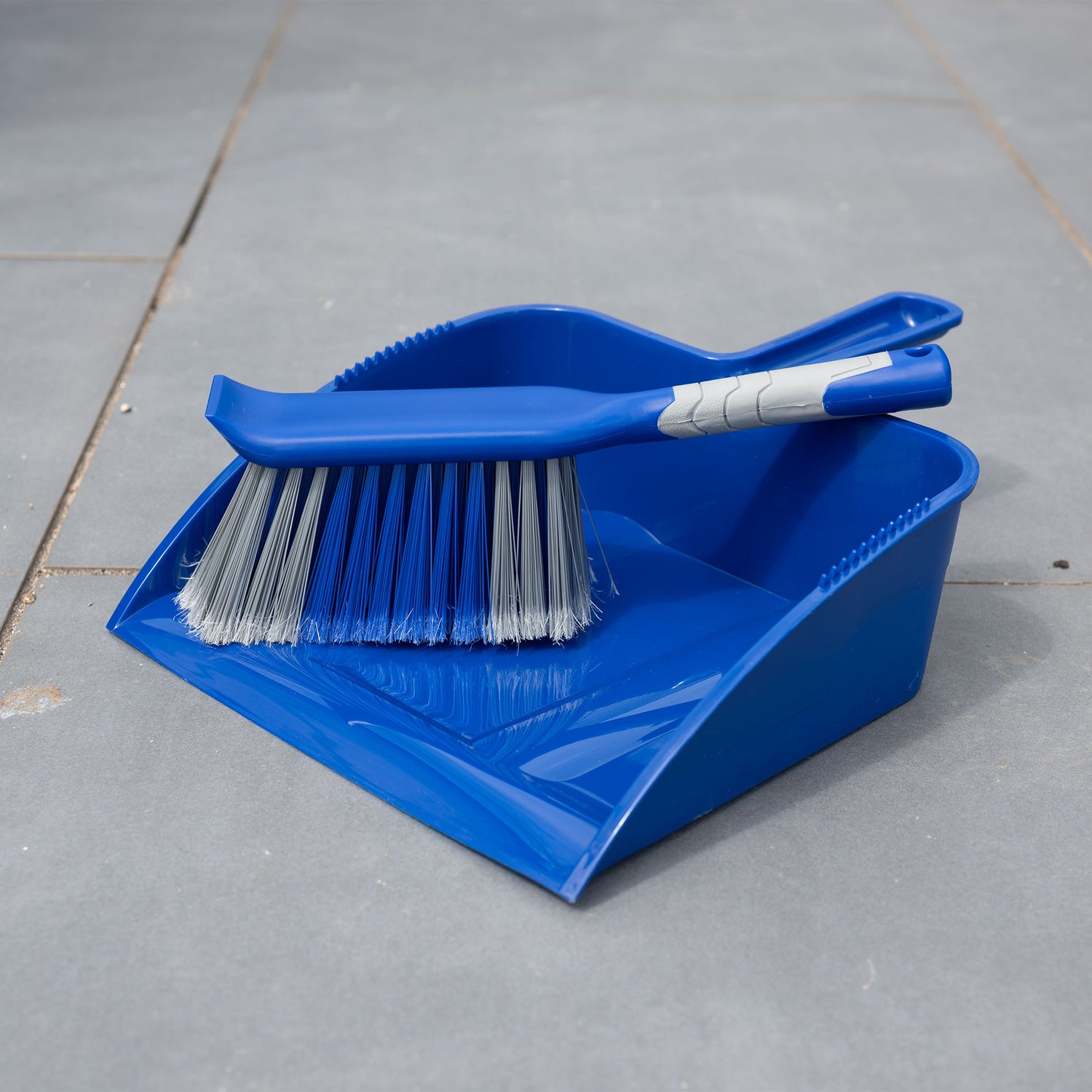 Blue dustpan and brush set on a gray tiled patio floor