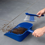 Person using a blue dustpan and brush to collect dirt on a gray floor.