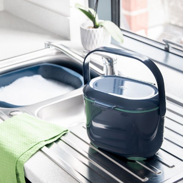 Dark Blue Plastic Compost Caddy sitting on a draining board by the sink in a kitchen.