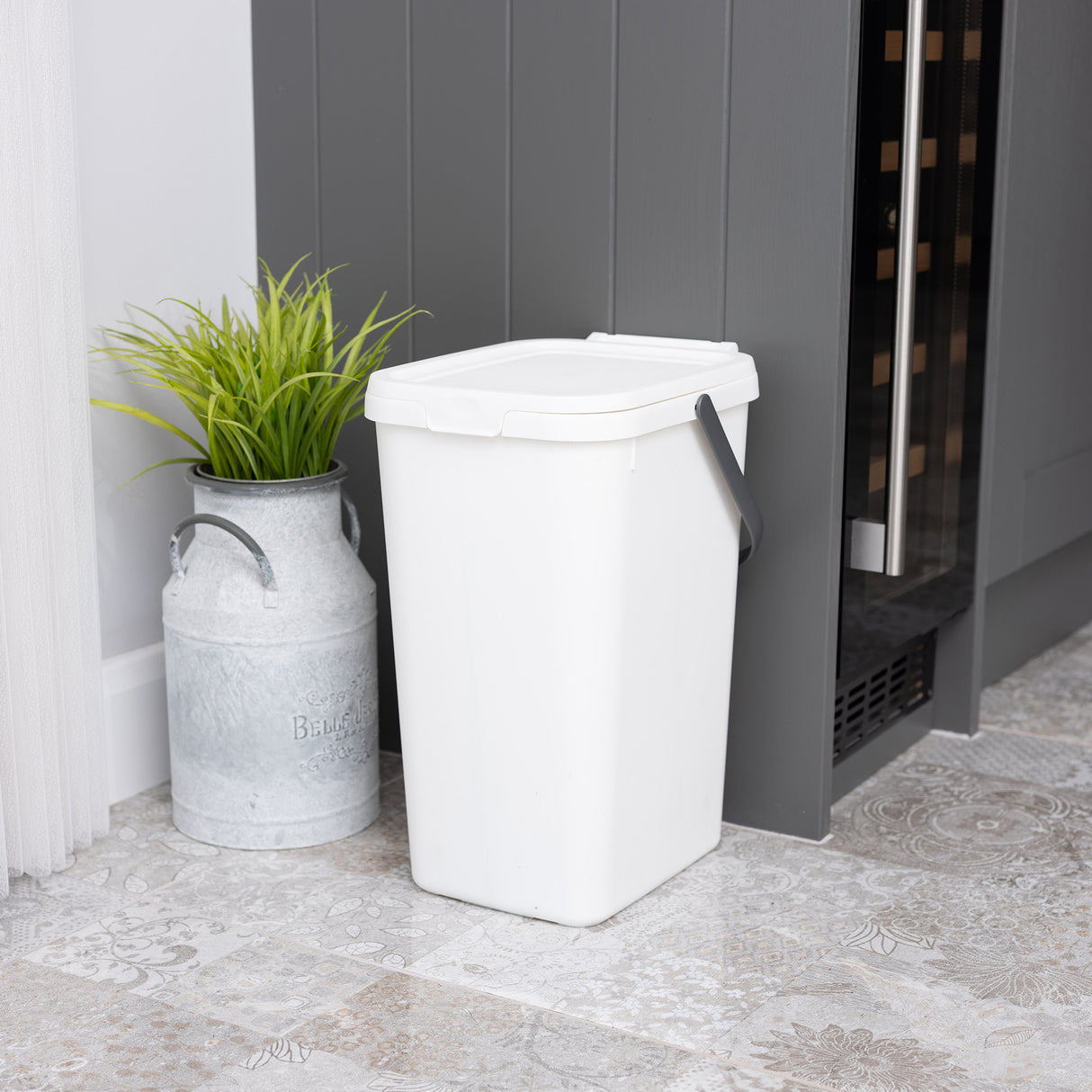 Small white utility caddy next to a grey cupboard with a plant in a metal pot.